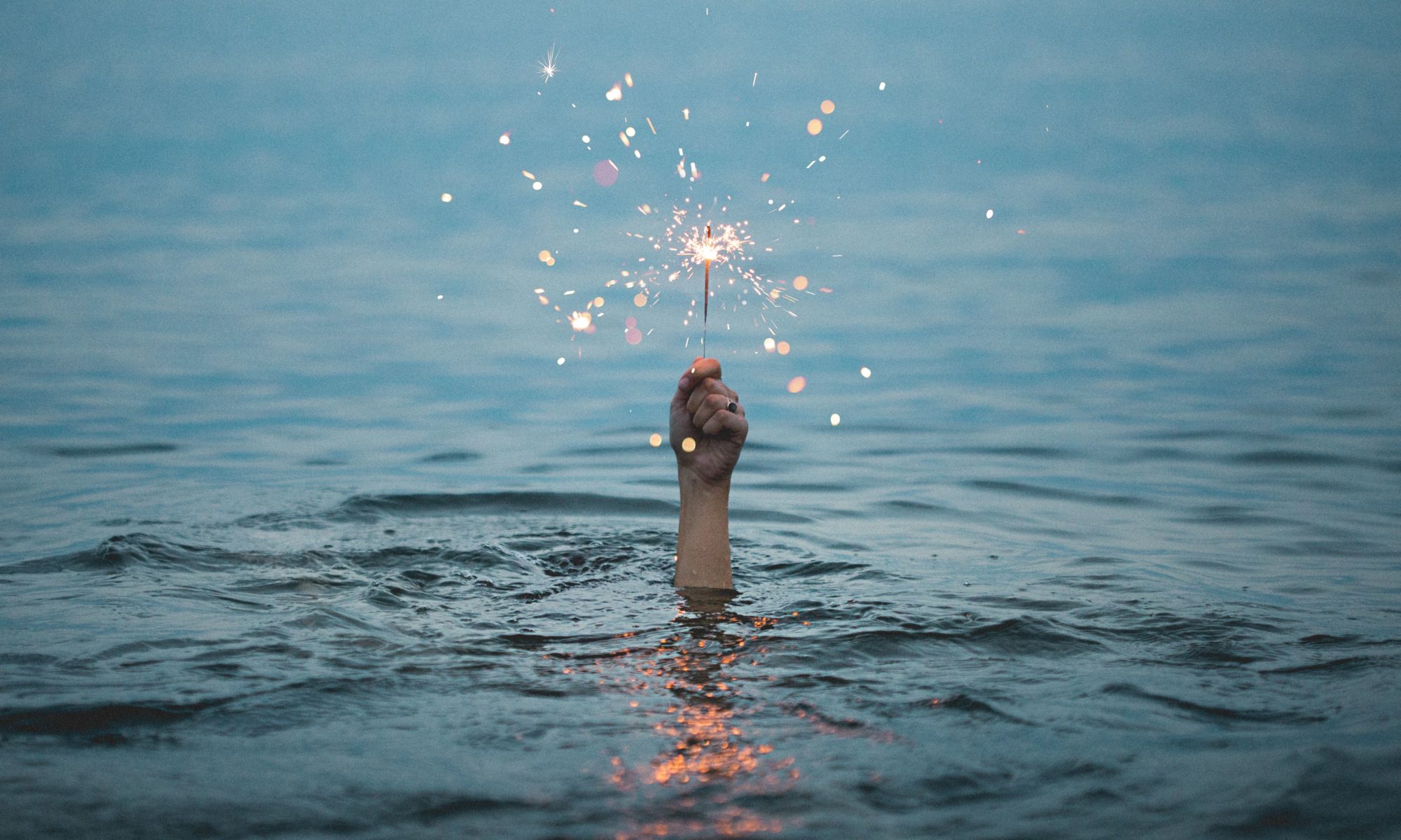 hand emerging from water holding a sparkler for blog Maslows Hierarchy of Needs